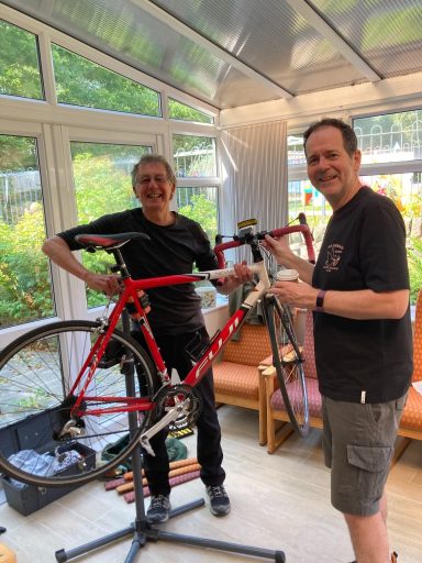 Two men working on a red bicycle in a bright, airy room.