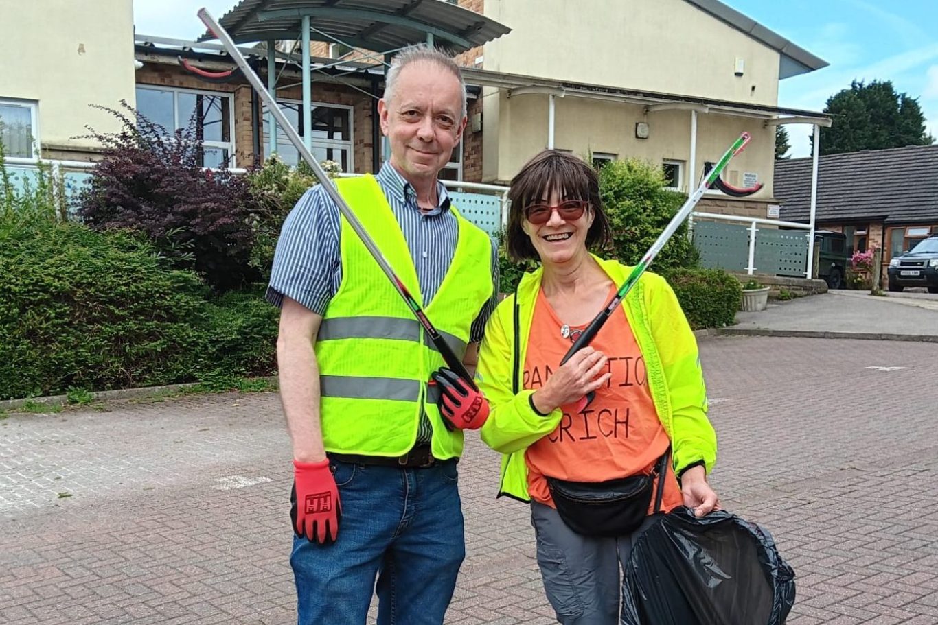 Two people in high-visibility vests holding litter pickers in a residential area.