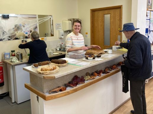 A smiling server assists a customer at a café counter with baked goods displayed.